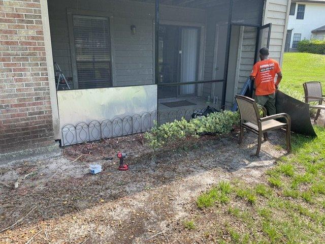 An AMWH worker in an orange company shirt repairing a screened porch panel on a brick house